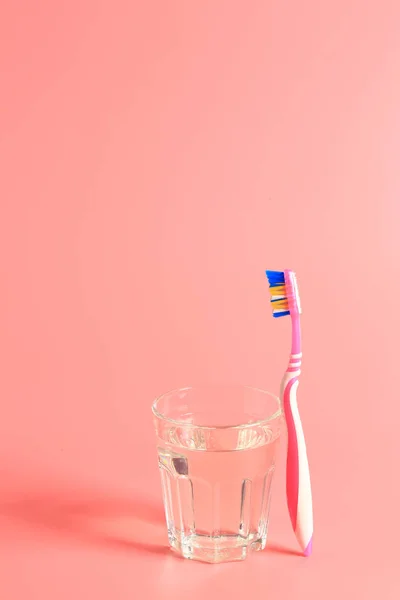 Tandborste och ett glas vatten på en rosa bakgrund — Stockfoto