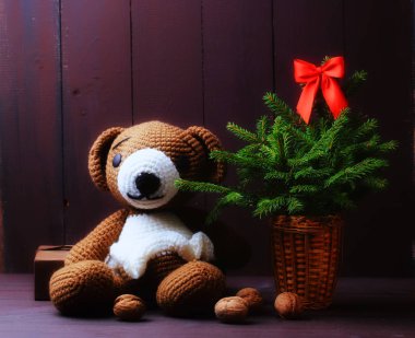 Noel arkaplanı. Örülmüş ayı oyuncağı, kırmızı yaylı ladin ve kahverengi arka planda ceviz.