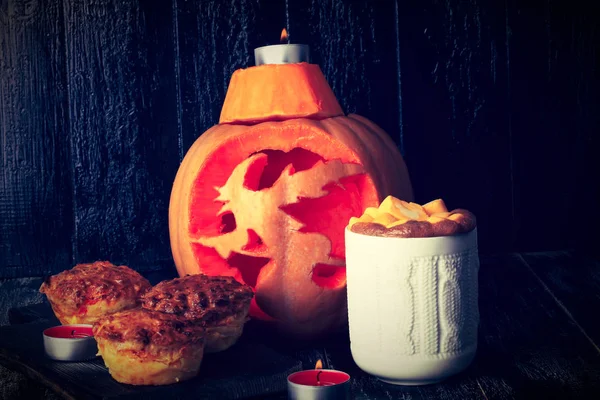 autumn composition with carved pumpkin, hot pumpkin spicy drink and muffins