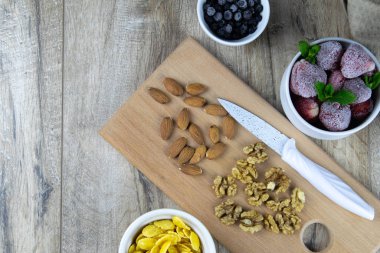 Bir kasede yulaf ezmesi ve müsli, ahşap zemin üzerinde taze böğürtlen ve süt ve üzerinde bıçak olan bir tahta.