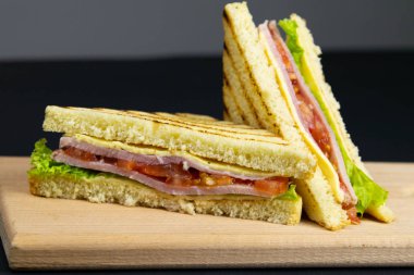 Tahta bir tahtanın üzerinde birkaç dilim beyaz ekmek. Sandviç peynirli ve jambonlu.