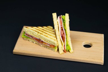 Tahta bir tahtanın üzerinde birkaç dilim beyaz ekmek. Sandviç peynirli ve jambonlu.