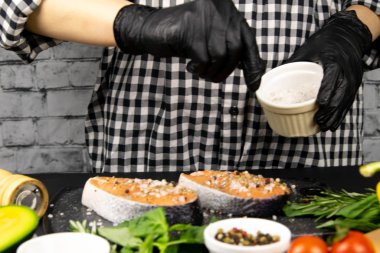 Eller yemek için somon bifteğini hazırlar ve tuzlar fesleğen, biberiye ve biberiyenin yanında.