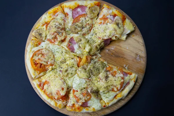 Піца з моцарелою, салямі, помідорами, бананами без жодного шматка, стоїть на дерев'яній дошці . — стокове фото