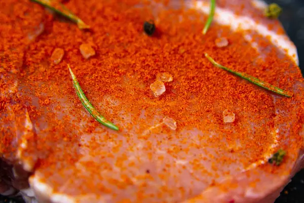 Rohes Schweinesteak auf Knochen, bestreut mit rotem Pfeffer in der Nähe von Rosmarin, Mais, Eiern und Paprika. — Stockfoto