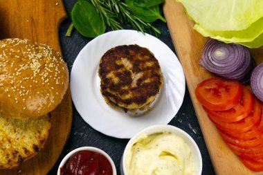 Ev yapımı hamburger malzemeleri: susamlı çörek, domates, mor soğan, lahana köftesi.