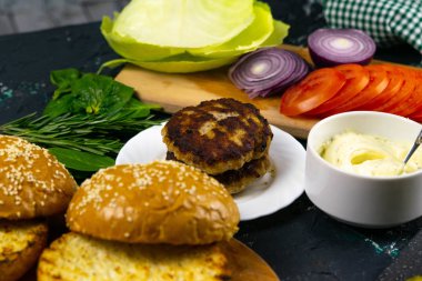 Ev yapımı hamburger malzemeleri: susamlı çörek, domates, mor soğan, lahana köftesi.