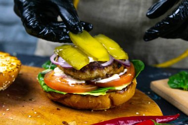 Hamburger pişirme süreci. Aşçı eldiveni ve hazırlanmış çizburgerli siyah eldiven.,