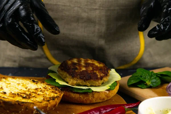 Hamburger pişirme süreci. Aşçı eldiveni ve hazırlanmış çizburgerli siyah eldiven.,