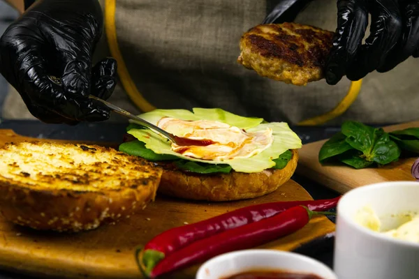 Hamburger pişirme süreci. Aşçı eldiveni ve hazırlanmış çizburgerli siyah eldiven.,