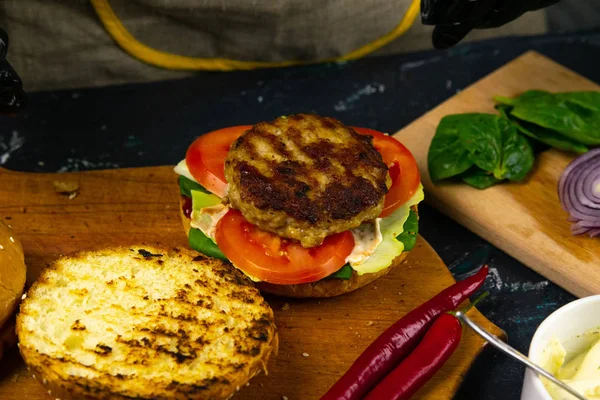 Hamburger pişirme süreci. Aşçı eldiveni ve hazırlanmış çizburgerli siyah eldiven.,