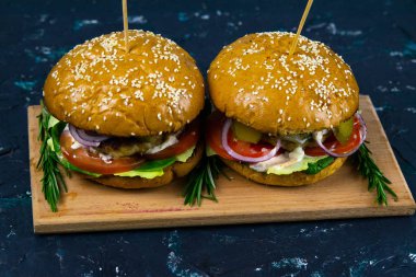 İki ev yapımı mantarlı sığır burger, mikro yeşiller, ahşap kesim tahtasındaki kırmızı soğan.