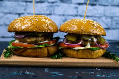 İki ev yapımı mantarlı sığır burger, mikro yeşiller, ahşap kesim tahtasındaki kırmızı soğan.