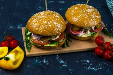 İki ev yapımı mantarlı sığır burger, mikro yeşiller, ahşap kesim tahtasındaki kırmızı soğan.