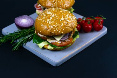 İki ev yapımı mantarlı sığır burger, mikro yeşiller, ahşap kesim tahtasındaki kırmızı soğan.