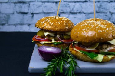 İki ev yapımı mantarlı sığır burger, mikro yeşiller, ahşap kesim tahtasındaki kırmızı soğan.