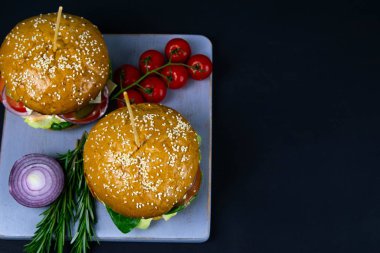 İki ev yapımı mantarlı sığır burger, mikro yeşiller, ahşap kesim tahtasındaki kırmızı soğan.