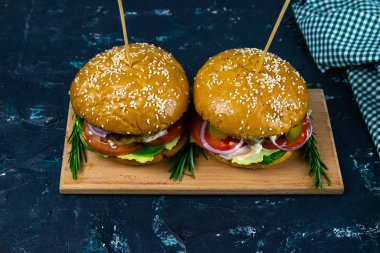 İki ev yapımı mantarlı sığır burger, mikro yeşiller, ahşap kesim tahtasındaki kırmızı soğan.