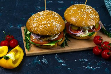 İki ev yapımı mantarlı sığır burger, mikro yeşiller, ahşap kesim tahtasındaki kırmızı soğan.