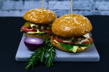 İki ev yapımı mantarlı sığır burger, mikro yeşiller, ahşap kesim tahtasındaki kırmızı soğan.