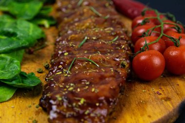 Barbecue Pork Spare Ribs close-up with tomatoes and basil as top view on an old cutting board