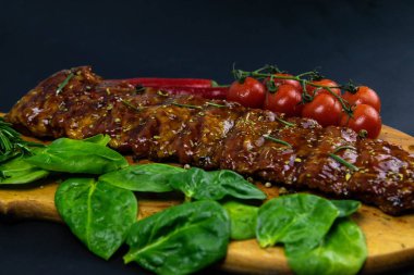 Barbecue Pork Spare Ribs as side view with basil and tomatoes on an old cutting board