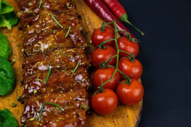 Barbecue Pork Spare Ribs as side view with basil and tomatoes and hot pepper on an old cutting board
