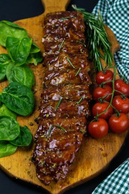Barbecue Pork Spare Ribs as side view with basil and tomatoes and hot pepper with cracker on an old cutting board