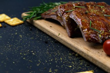 Barbecue Pork Spare Ribs as side view with basil and tomatoes and hot pepper with cracker on an old cutting board
