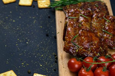 Barbecue Pork Spare Ribs as side view with basil and tomatoes and hot pepper with cracker on an old cutting board