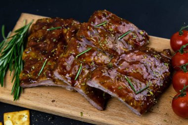 Barbecue Pork Spare Ribs as side view with rosemary and tomatoes and hot pepper on an old cutting board