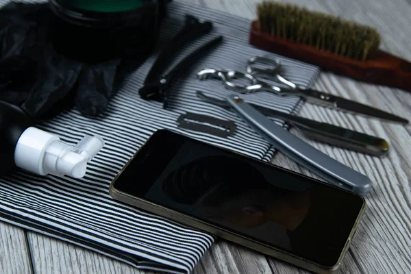 Las herramientas del barbero se colocan en una toalla a rayas al lado del teléfono con una foto de un corte de pelo hecho al cliente . — Foto de Stock