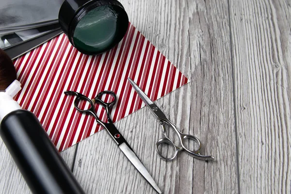 Scissors, shaving gel and hair gel stand on a stack of magazines which stands on a gray wood table