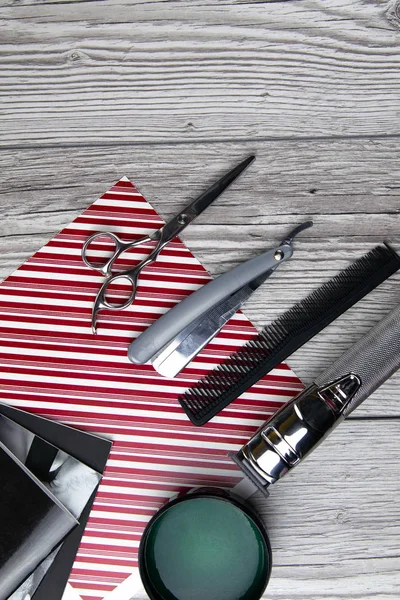 Ножницы, гель для бритья и гель для волос стоят на стопке журналов, которые стоят на сером деревянном столе — стоковое фото