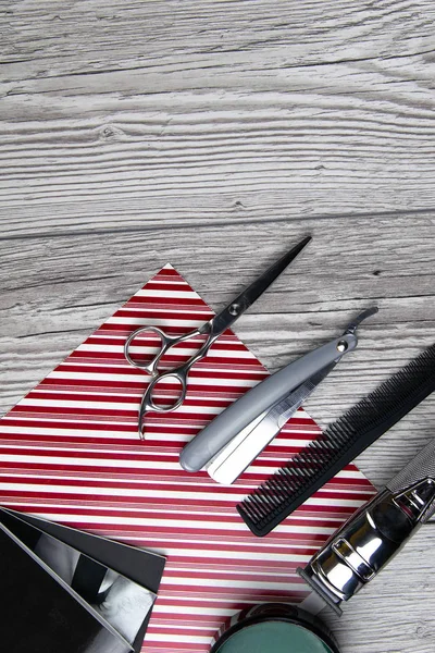 Scissors, shaving gel and hair gel stand on a stack of magazines which stands on a gray wood table