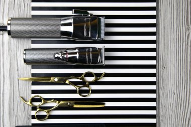 Saç kesim makineleri, farklı boyutlarda hortumlar, taraklar ve jeller, güzel siyah beyaz çizgiler üzerine serilmiş.