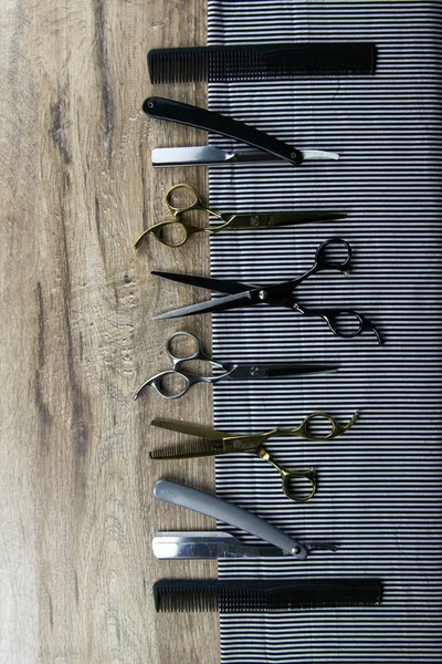 A set of scissors for haircuts, combs and a dangerous razor spread on a striped towel that stands on a wooden table — 스톡 사진