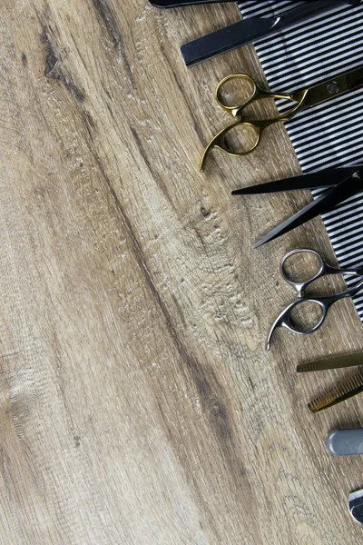 Un conjunto de tijeras para cortes de pelo, peines y una peligrosa cuchilla extendida sobre una toalla a rayas que se apoya sobre una mesa de madera — Foto de Stock