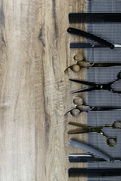 Un conjunto de tijeras para cortes de pelo, peines y una peligrosa cuchilla extendida sobre una toalla a rayas que se apoya sobre una mesa de madera — Foto de Stock