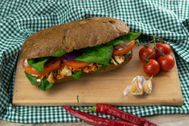 Tavuklu, domatesli, ıspanaklı, peynirli ve havuçlu bir sandviç tahta bir tahtanın üzerinde duruyor.