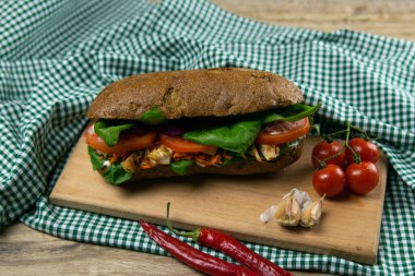 Tavuklu, domatesli, ıspanaklı, peynirli ve havuçlu bir sandviç tahta bir tahtanın üzerinde duruyor.