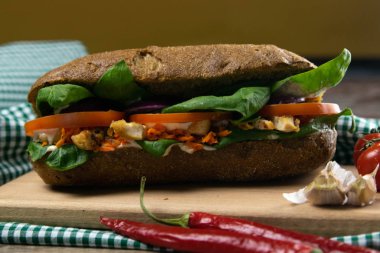 Tavuklu, domatesli, ıspanaklı, peynirli ve havuçlu bir sandviç tahta bir tahtanın üzerinde duruyor.