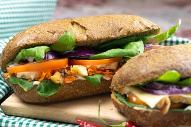 Tavuklu, domatesli, ıspanaklı, peynirli ve havuçlu bir sandviç tahta bir tahtanın üzerinde duruyor.