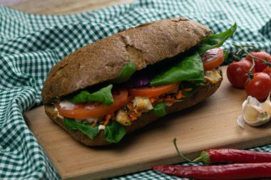 Tavuklu, domatesli, ıspanaklı, peynirli ve havuçlu bir sandviç tahta bir tahtanın üzerinde duruyor.