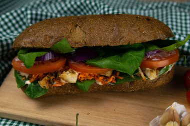 Tavuklu, domatesli, ıspanaklı, peynirli ve havuçlu bir sandviç tahta bir tahtanın üzerinde duruyor.