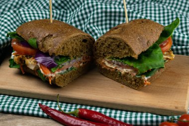 Tavuklu, domatesli, ıspanaklı, peynirli ve havuçlu bir sandviç tahta bir tahtanın üzerinde duruyor.