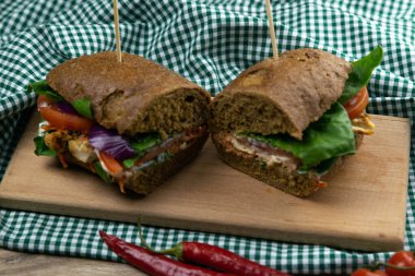 Tavuklu, domatesli, ıspanaklı, peynirli ve havuçlu bir sandviç tahta bir tahtanın üzerinde duruyor.