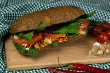 Tavuklu, domatesli, ıspanaklı, peynirli ve havuçlu bir sandviç tahta bir tahtanın üzerinde duruyor.