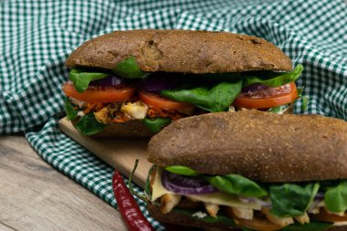 Tavuklu, domatesli, ıspanaklı, peynirli ve havuçlu bir sandviç tahta bir tahtanın üzerinde duruyor.