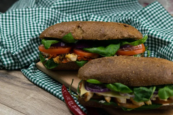 Tavuklu, domatesli, ıspanaklı, peynirli ve havuçlu bir sandviç tahta bir tahtanın üzerinde duruyor.